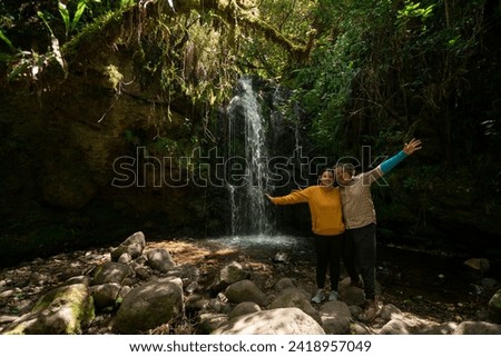 Portrait of a young couple taking photos next to a waterfall in the middle of a forest during a sunny day