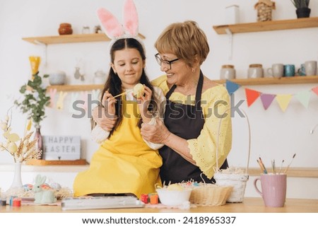 Happy easter! A grandmother and her granddaughter painting Easter eggs. Happy family preparing for Easter. Cute little child girl wearing bunny ears on Easter day.