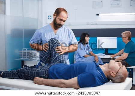 Retired old man with knee injury receiving osteopathic assistance for physical recovery. Healthcare assistant massaging senior patient with leg muscle pain, helping to relieve pressure. Royalty-Free Stock Photo #2418983047