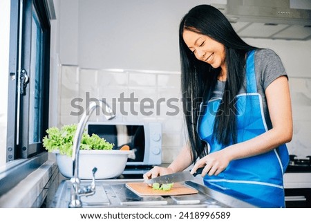 Close-up of a smiling woman in an apron cutting vegetables for a healthy salad. Emphasizing the housewife's preparation of a nutritious meal for dinner. Royalty-Free Stock Photo #2418996589