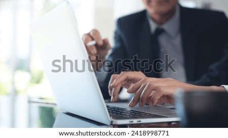 Two asian business persons working together. Businessman brainstorming, having a discussion with his colleague about work project, working on laptop computer at modern office. Business teamwork