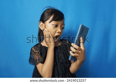 photo of young shocked impressed little girl kid child hold smartphone cellphone isolated on blue color background
