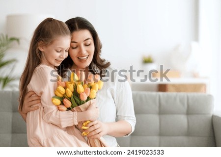Happy mother's day. Child daughter is congratulating mom and giving her flowers. Mum and girl smiling and hugging. Family holiday and togetherness.