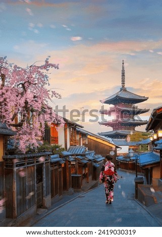 Scenic cityscape of Yasaka pagoda sunset in Kyoto with a young Japanese woman in a traditional Kimono dress during full bloom cherry blossom and scatter sakura petals Royalty-Free Stock Photo #2419030319