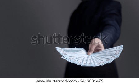Dollar banknote being handed over from the hand of a businessman on a dark background. Royalty-Free Stock Photo #2419031475