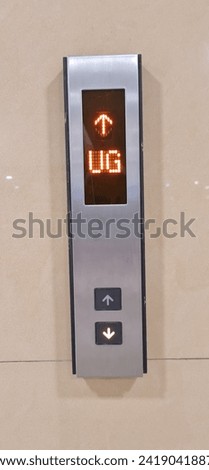 The push button for going up and down the elevator is usually located on the side wall of the elevator door. The sign is showing the direction up and the elevator is on floor UG.