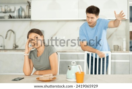 Annoyed young girl sitting sadly while guy is brawling with her in the kitchen Royalty-Free Stock Photo #2419065929
