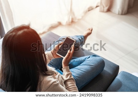 Young woman using smart phone and relaxing on sofa in living room at cozy home in the morning