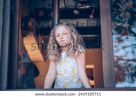 adorable girl with long blond hair looking through window