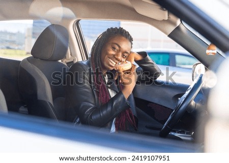 View from outside the window of a smiling cute african woman eating pastries inside a car