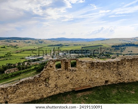 Picturesque view of old city from from observation deck of ancient Rupea fortress in Romania against cloudy sky. Fortress was built on ruins of former Dacian defensive structure. Copy space. Royalty-Free Stock Photo #2419110091