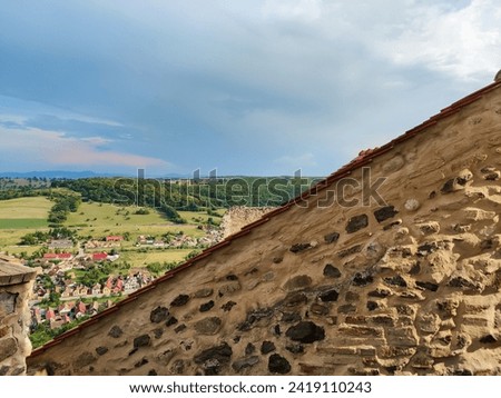 Picturesque view of old city from from observation deck of ancient Rupea fortress in Romania against cloudy sky. Fortress was built on ruins of former Dacian defensive structure. Copy space. Royalty-Free Stock Photo #2419110243