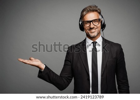 Adult employee operator business man wears black suit set microphone headset for helpline assistance sit work at call center office desk with pc computer isolated on grey background studio portrait Royalty-Free Stock Photo #2419123789
