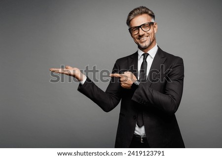 Adult successful employee business man corporate lawyer wear classic formal black suit shirt tie work in office point index finger on empty area palm isolated on plain grey background studio portrait Royalty-Free Stock Photo #2419123791