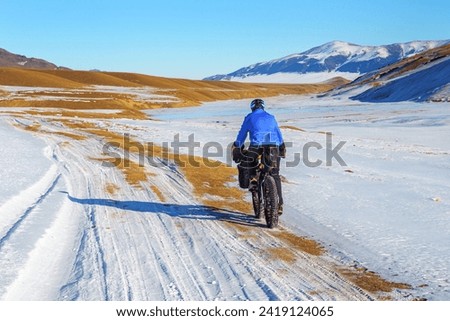 A male traveler rides a fat bike in the mountains in winter. Winter trip. High mountain plateau Turgen-Asy, Kazakhstan. Royalty-Free Stock Photo #2419124065