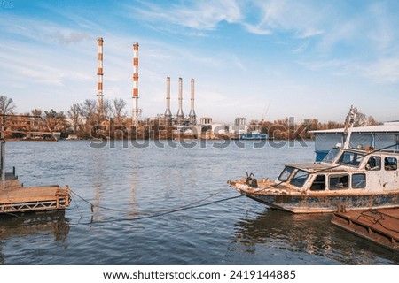A factory by the river emits pollution into the water, with rusty ships and industrial infrastructure symbolizing the environmental impact of industrial activity on the ecosystem.