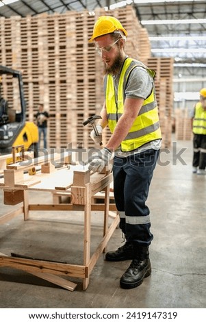 Confident production worker busy working at lumber warehouse of wooden furniture factory. Skilled technician wears safety hardhat standing in hardwood plank manufacturing facility using serious tool.