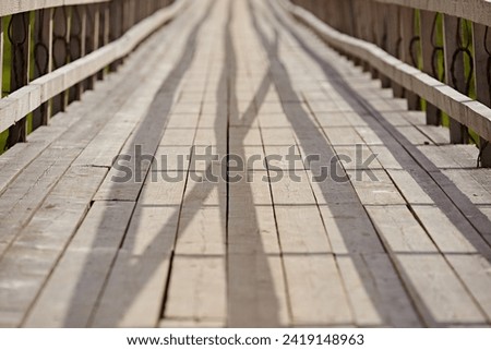 Suspended bridge with wooden fences, footpath from planks, close-up. Abstract lines go into perspective. Shadows fall on the surface from the sun. Symmetric abstract objects