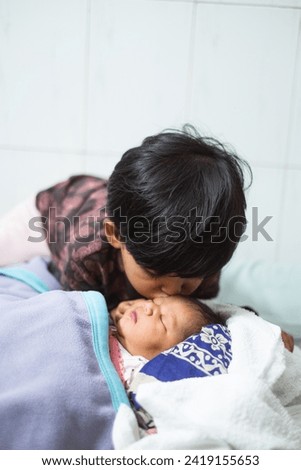 South asian little girl kissing her newborn sister in forehead with love 