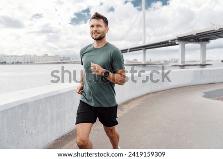 Man running by the river with a bridge in the background, focused on his fitness.
