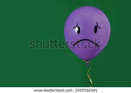 Purple balloon with sad face on green background. Space for text