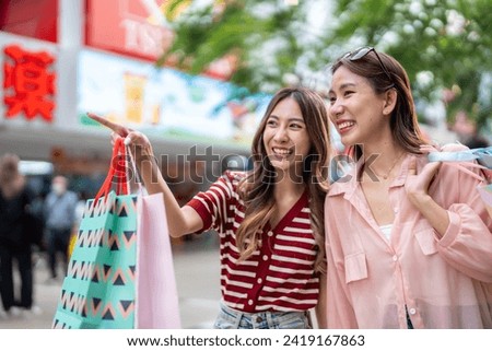 Asian young women shopping goods outdoor in shopping street at night. Attractive young female friends holding shopping bags then walking with happiness enjoy purchasing in department store together.