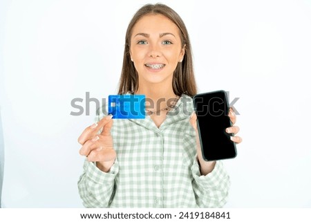 Photo of adorable Young beautiful woman wearing green plaid pyjama holding credit card and Smartphone. Reserved for online purchases