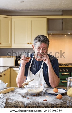 Cookery lessons. A humorous picture of a attempting to cook as he gives up and has a drink. Kitchen image of food preparation and cooking.