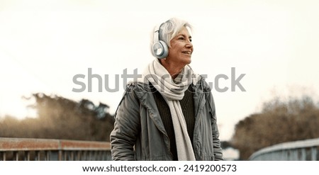 Senior woman, headphones and music outdoor, walking and wellness with audio streaming and energy. Podcast, listen to radio and sound with female person on city bridge, exercise and travel with tech