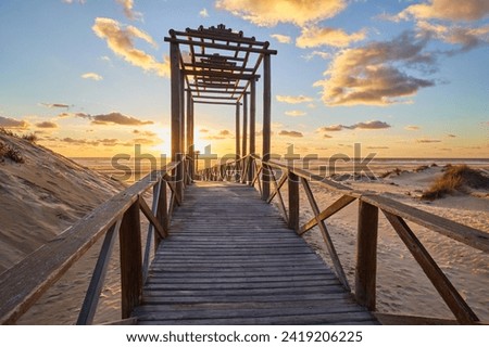 Dramatic sea sunset. The blinding sun hid behind the arch of the wooden bridge. The setting sun sinks into the sea