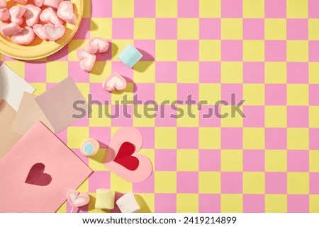 Creative background for design on valentine’s day. Yellow plates with sweet marshmallow decorated with color paper card on pink and yellow checkered background. Copy space
