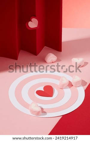 Women's day and Valentine's day concept with a bullseye in pink and white color decorated with several heart-shaped marshmallows. Red paper heart origami featured. Template for design