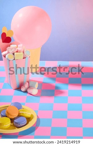 Valentine day concept for design. Front view of dish and box filled with sweet marshmallow and cakes decorated on color checkered background. Space for design and display product
