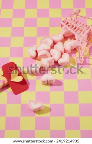 Pink mini trolley with sweet marshmallow in heart shape decorated on pink and yellow checkered background. Cute decorations for valentine's day. Copy space