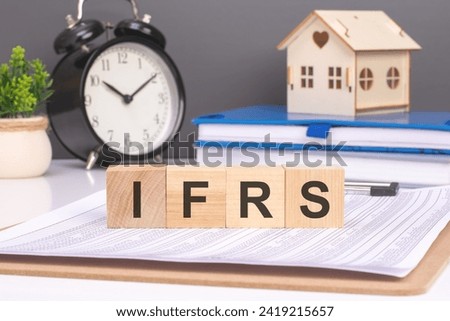ifrs word in wooden blocks with small wooden house and alarm clock on background. idea of incorporating International Financial Reporting Standards into the foundation of business operations