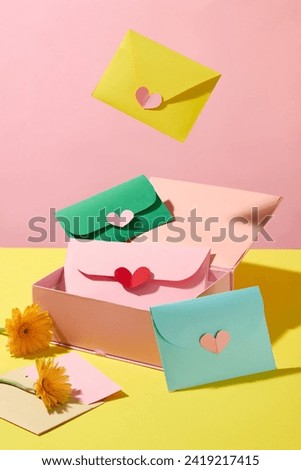 On a pink background, a pink gift box with cute cards is flying, decorated with fresh gerberas. Concept of making your own cards with meaningful wishes for International Women's Day