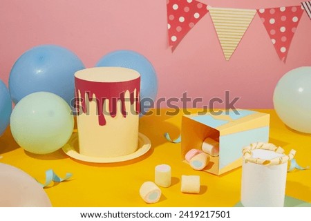 Birthday party with a birthday cake made from paper, marshmallows and balloons on a yellow surface. A triangular flag string decorated on a pink background.