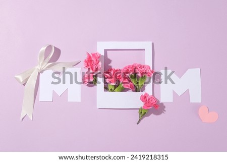 Two letters and a paper frame combined form the word Mom. Many flowers in pink color decorated with a ribbon bow and a paper heart. Banner or leaflet for March 8