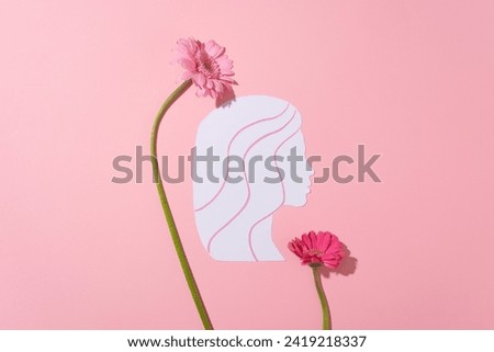 International Women's Day concept with a white paper cut in a woman shaped decorated with fresh flowers in pink color on the surface. Top view. A day to call for positive change advancing women