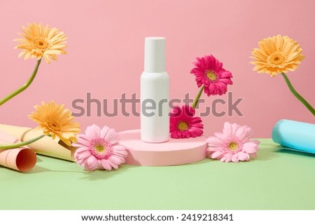 Front view of an unlabeled white cosmetic bottle displayed on a podium. The surrounding is decorated with bright gerbera flowers on a pastel background. Royalty-Free Stock Photo #2419218341