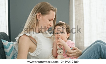 Mother and daughter sitting on sofa sucking toy at home