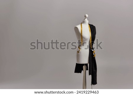 mannequin on tripod with quality fabric and measuring tape on grey background, dressmaking business
