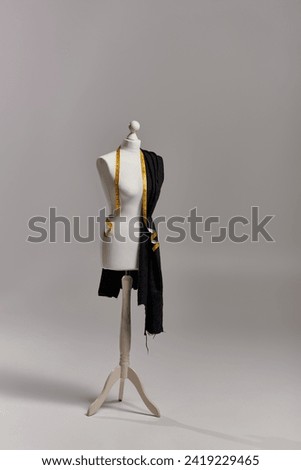 mannequin on tripod with fabric and measuring tape on grey backdrop, fashion business concept
