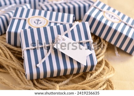 Wedding favours nautical style decoration soap guest gifts, wrapped in blue white striped pattern paper, cotton ribbon, custom label, sailor rope background, original summer beach party souvenir Royalty-Free Stock Photo #2419236635