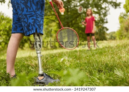 Low section of boy with amputated leg playing badminton at park