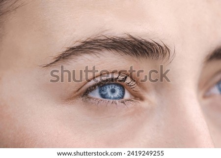 Blue eyes of young woman with black eyelashes looking away, no make up, dry facial skin, human eye supermacro, closeup background, soft focus
