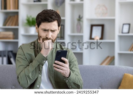 Close-up of mature man upset and disappointed received online news notification message on phone, bad daughter-in-law, sitting on sofa in living room at home. Royalty-Free Stock Photo #2419255347