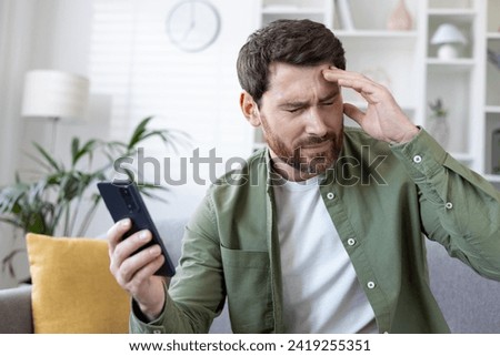Close-up of mature man upset and disappointed received online news notification message on phone, bad daughter-in-law, sitting on sofa in living room at home. Royalty-Free Stock Photo #2419255351