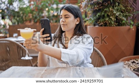 Young beautiful hispanic woman taking picture to a tropical cocktail drink at bar terrace