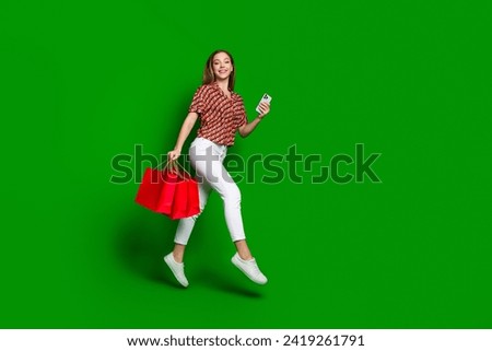 Full size photo of beautiful carefree teenager hold shopping bags make purchase with smartphone isolated on green color background
